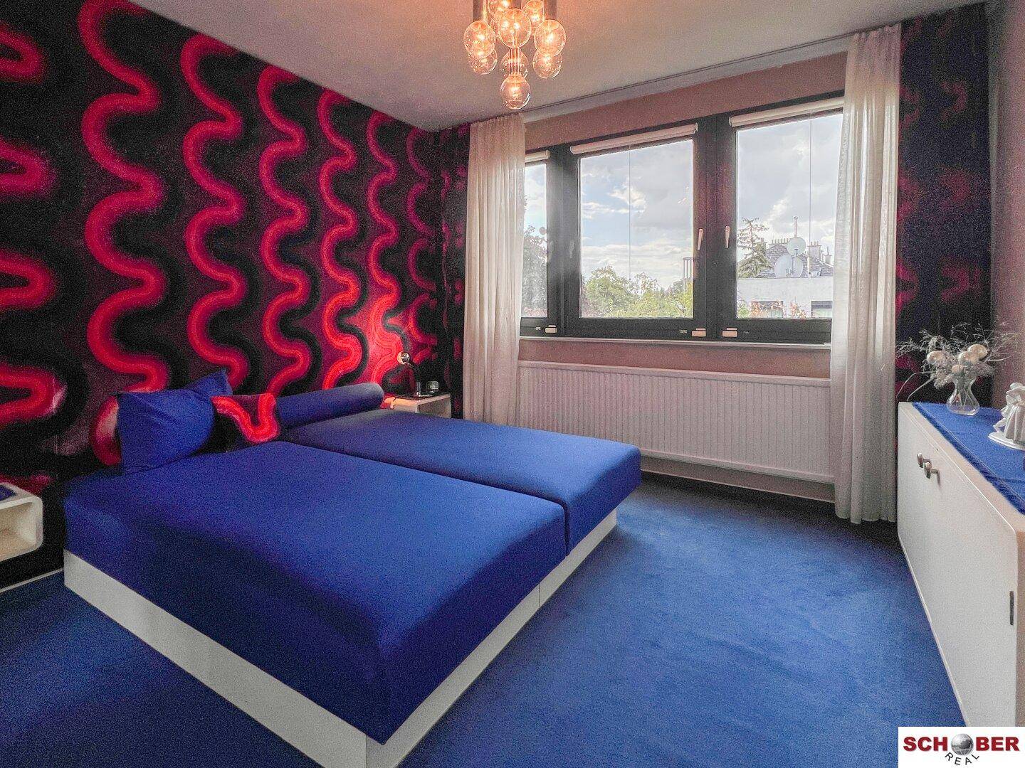 Schlafzimmer mit zwei Einzelbetten, auffälliger rot-schwarzer Tapete und einem Fenster.