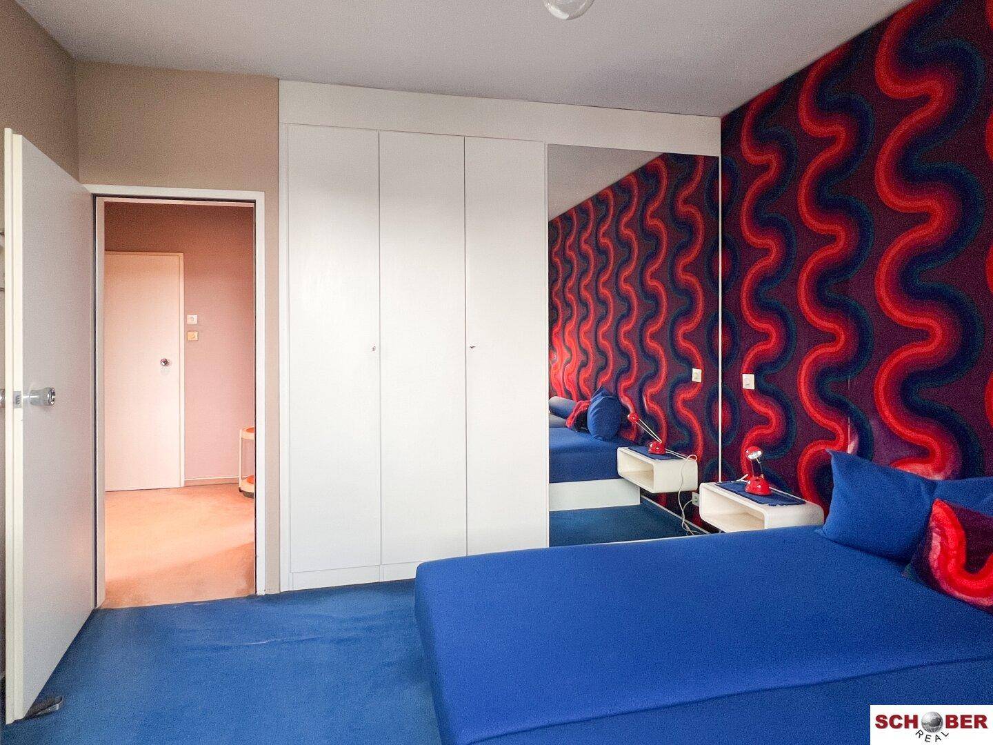 Schlafzimmer mit zwei Einzelbetten, auffälliger Tapete und weißen Einbauschränken mit Spiegeltüren.