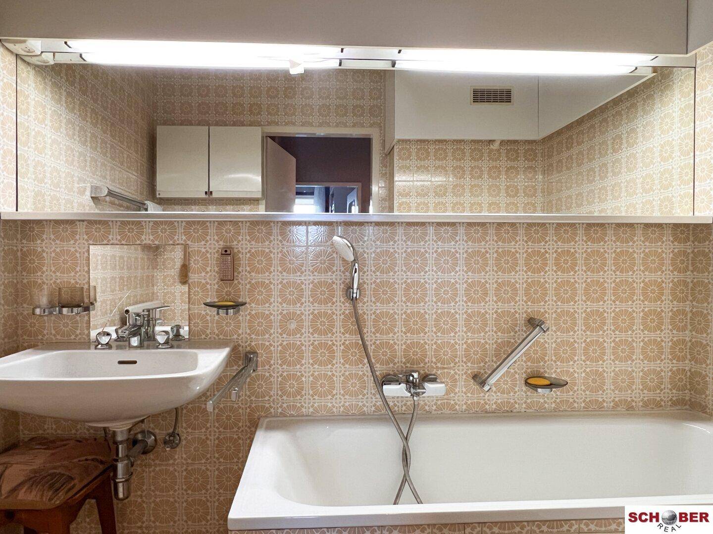 Badezimmer mit Waschbecken, Spiegel und Badewanne, verziert mit gemusterten beigefarbenen Fliesen.