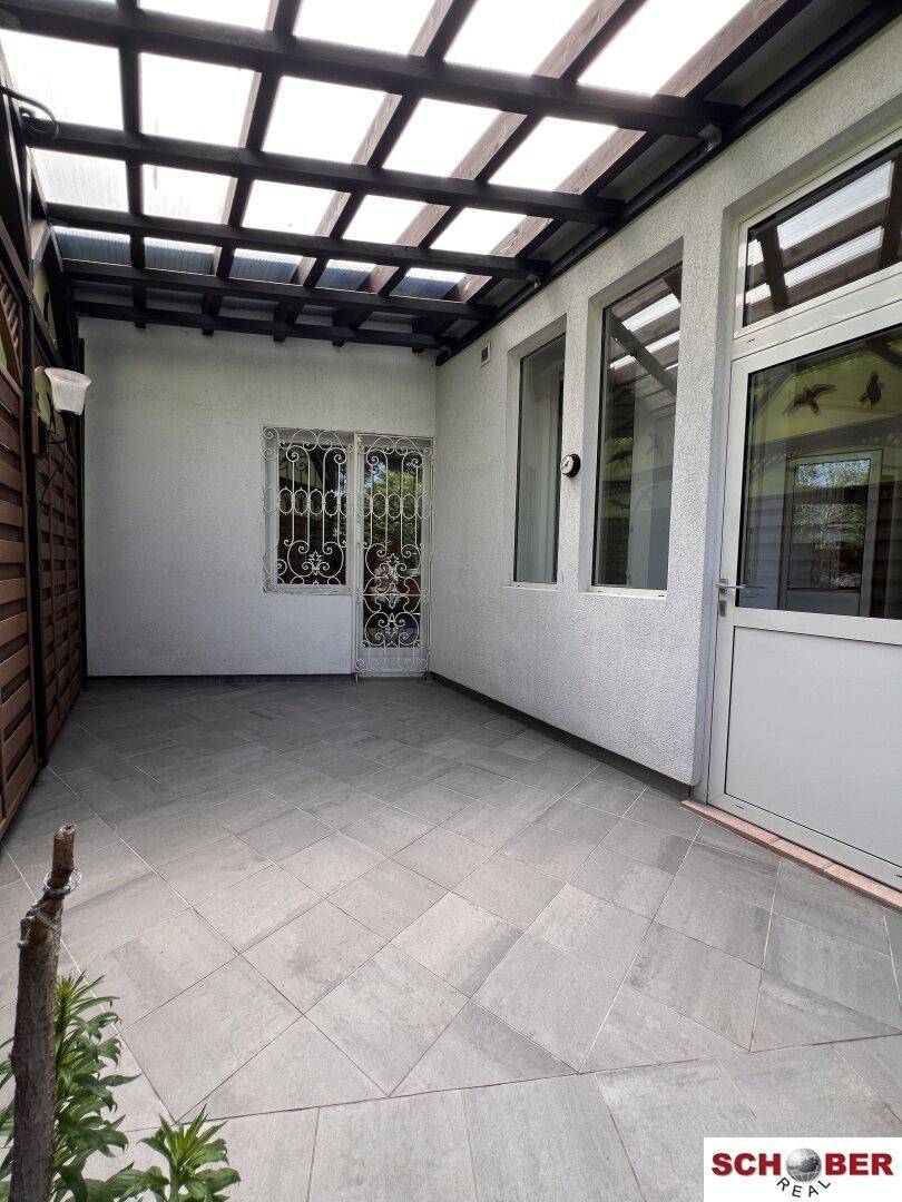Überdachte Terrasse mit modernen grauen Fliesen und Zugang zum Innenbereich, bietet Schutz vor Witterung.