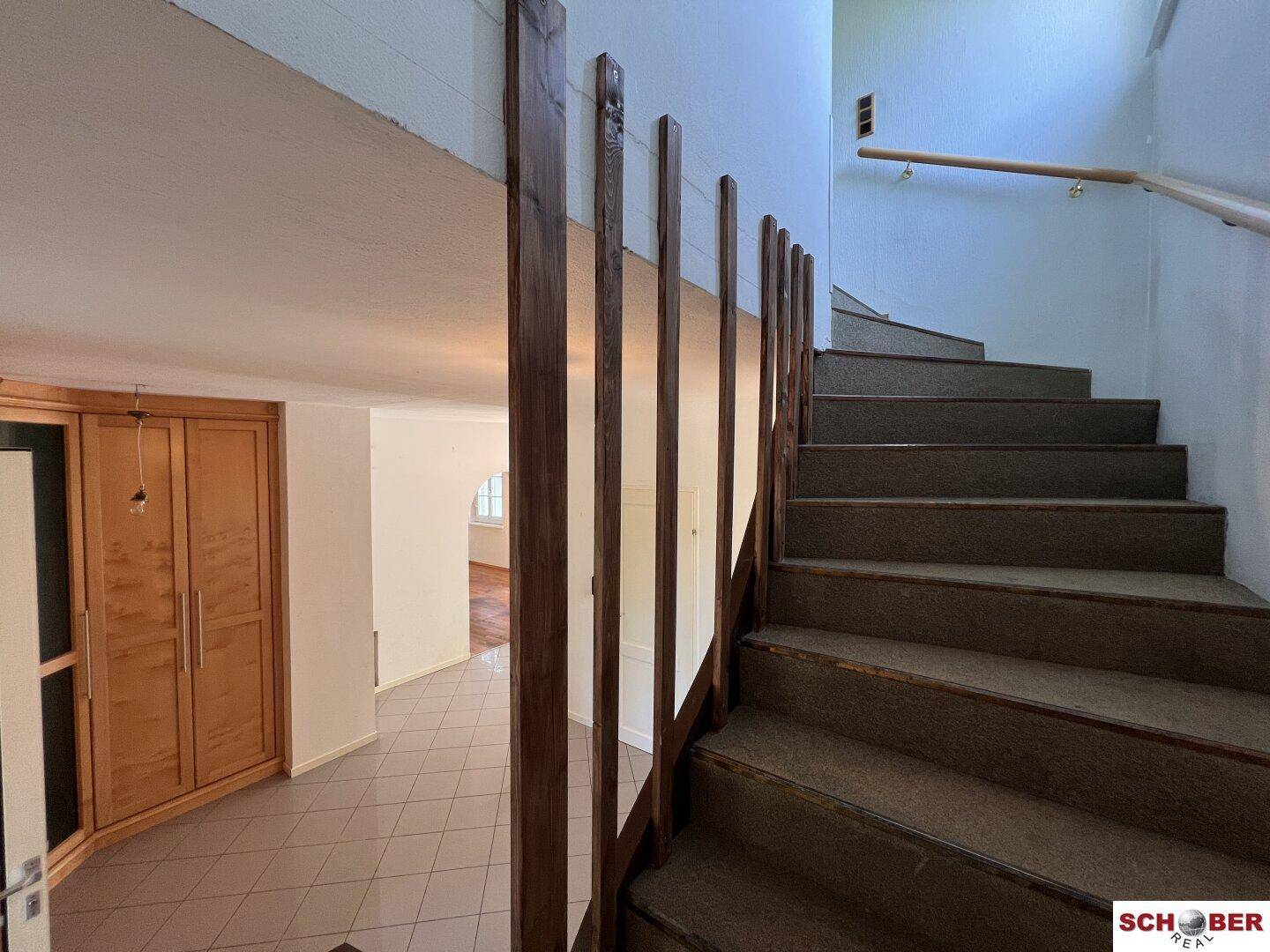 Treppenhaus mit Teppichstufen und Holzgeländer, angrenzend an einen gefliesten Eingangsbereich.