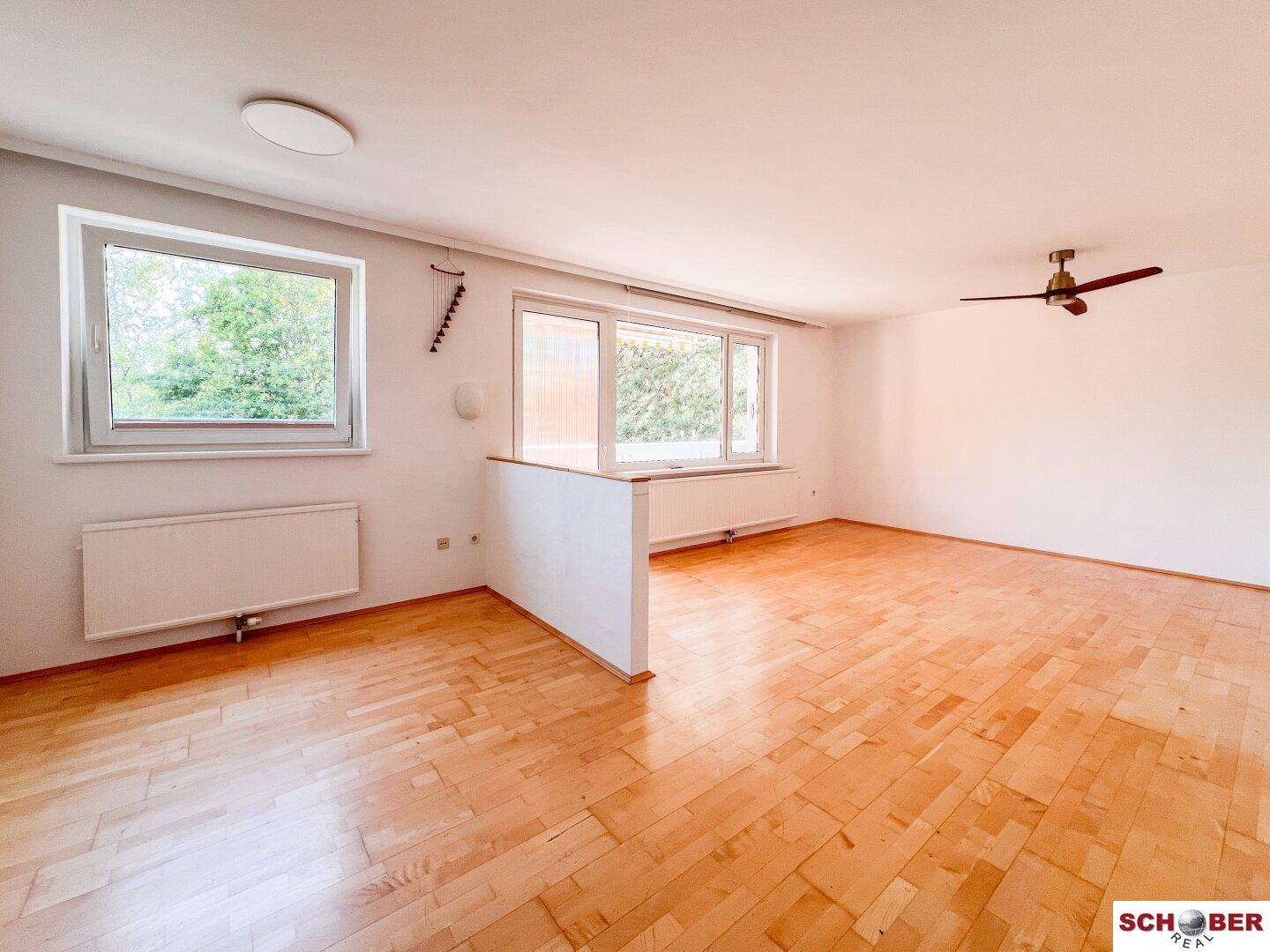 Geräumiger, heller Wohnraum mit Parkettboden, großen Fenstern und Deckenventilator.