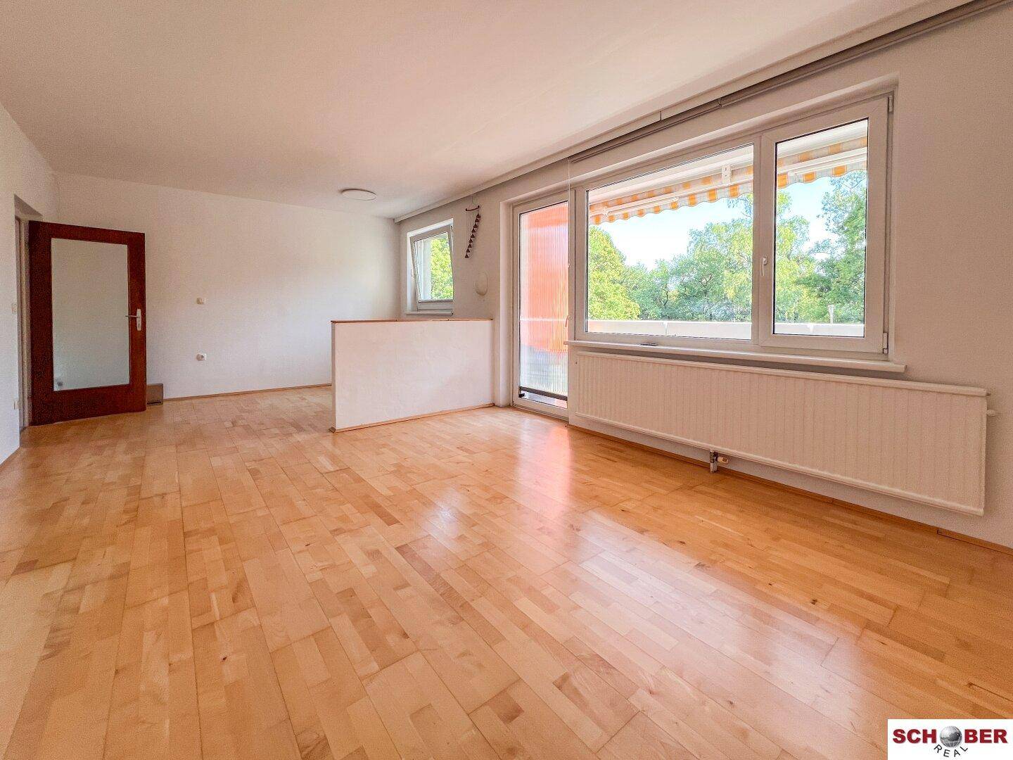 Heller Wohnbereich mit Parkettboden und direktem Zugang zum sonnigen Balkon.