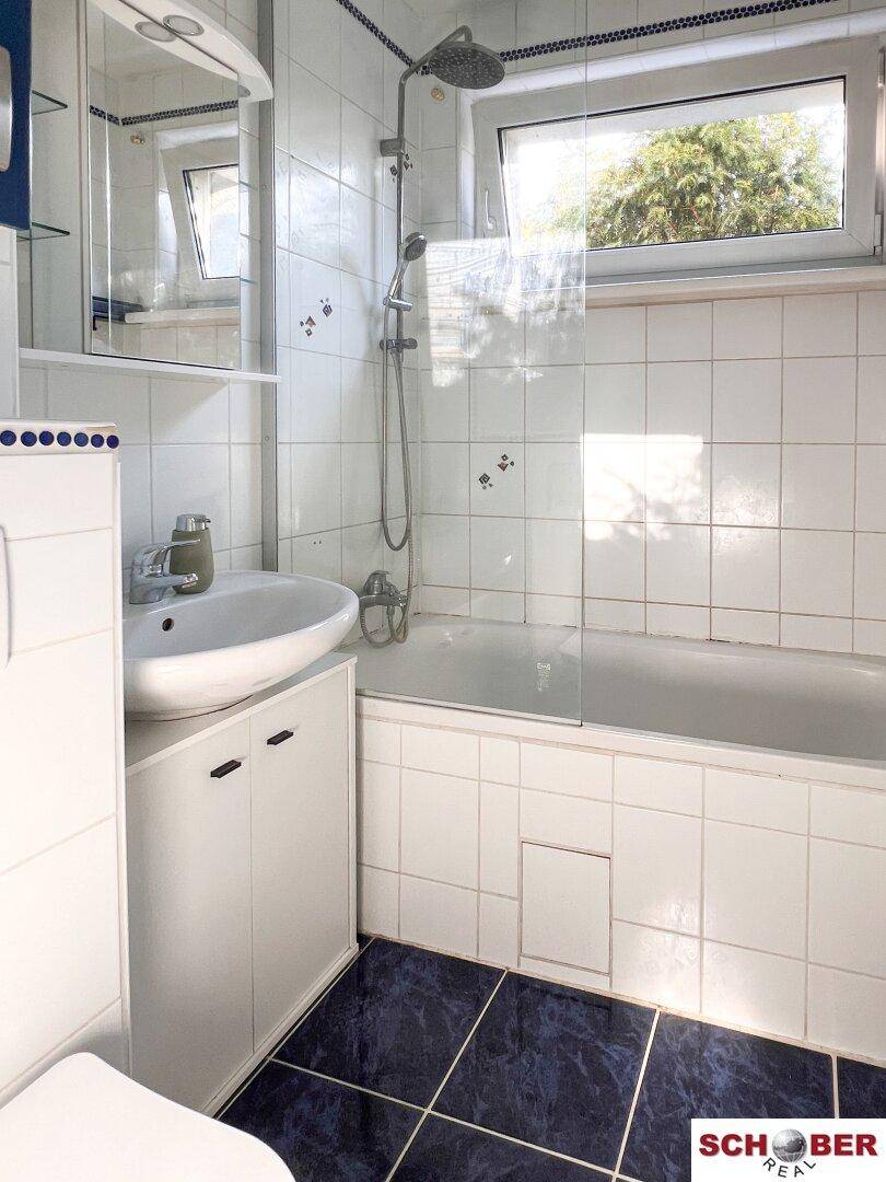 Badezimmer mit Badewanne, Waschbeckenunterschrank und Fenster, hell gefliest.