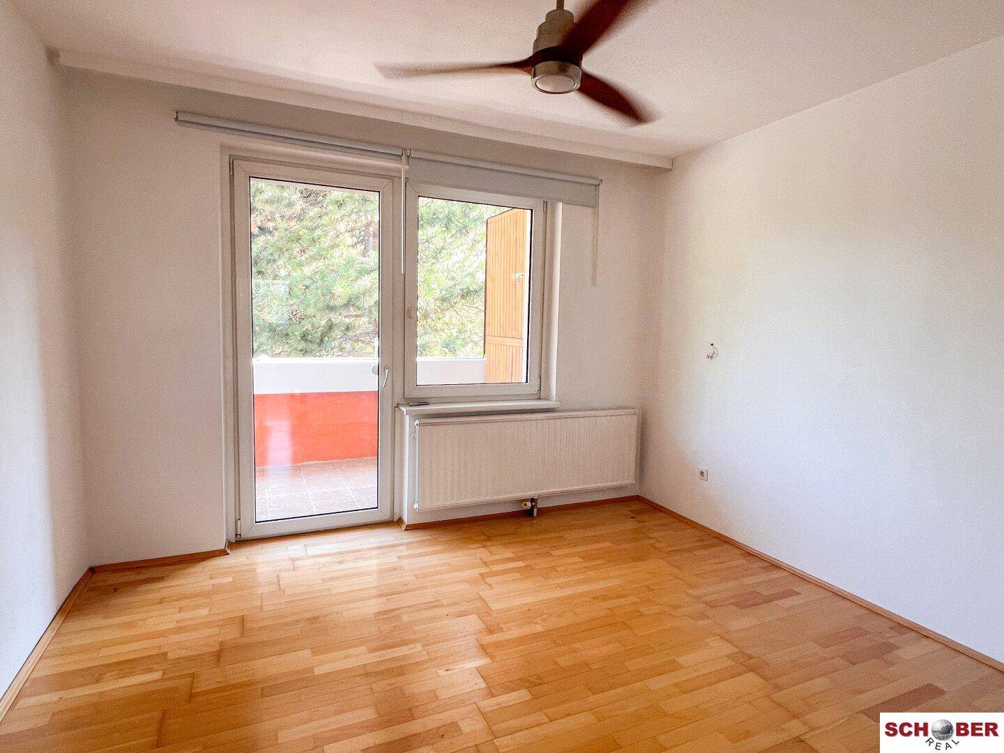 Helles Schlafzimmer mit Parkettboden, Balkonzugang und Deckenventilator.