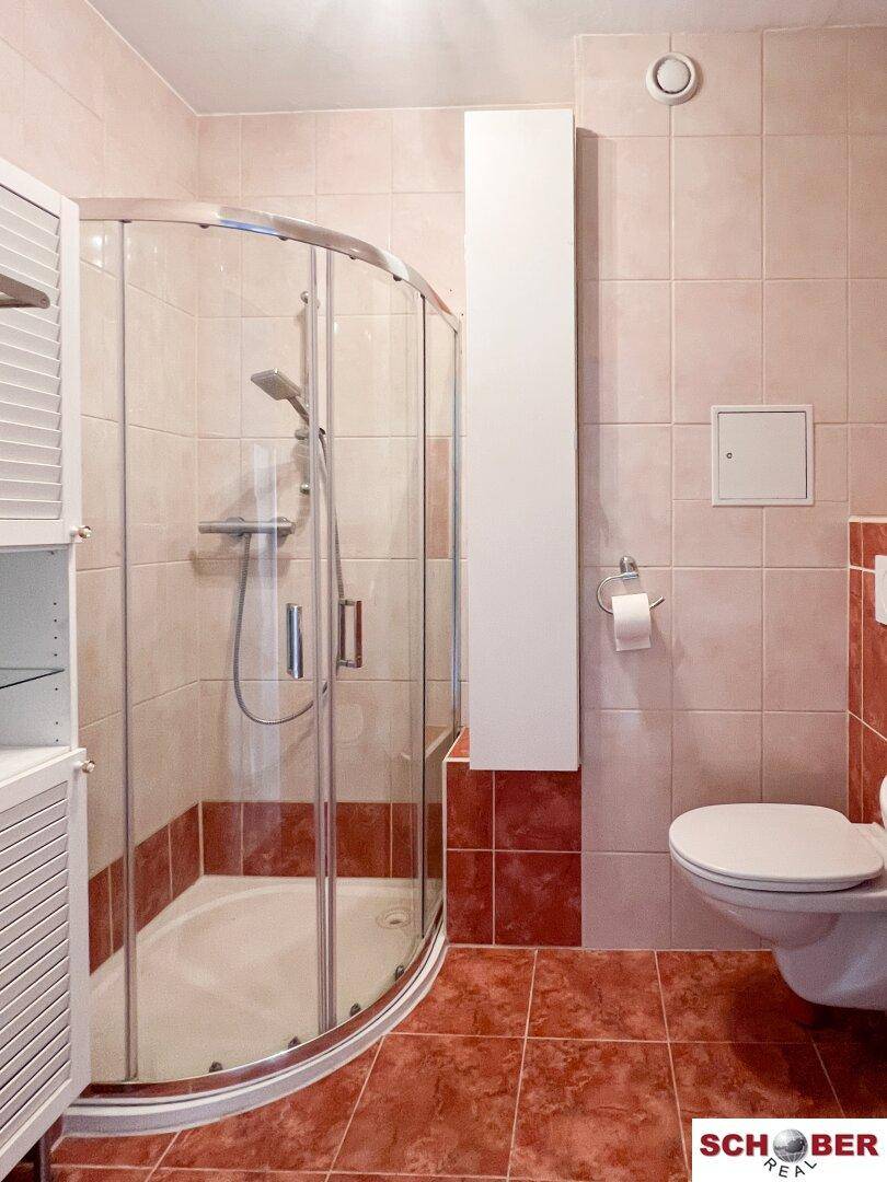 Badezimmer mit Duschkabine, wandhängendem WC und roten Fliesen.