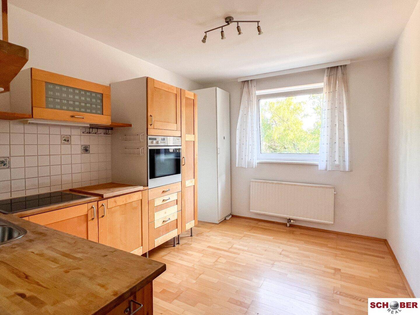 Funktionale Küche mit hellen Holzschränken, Einbauofen und Fenster mit Blick ins Freie.