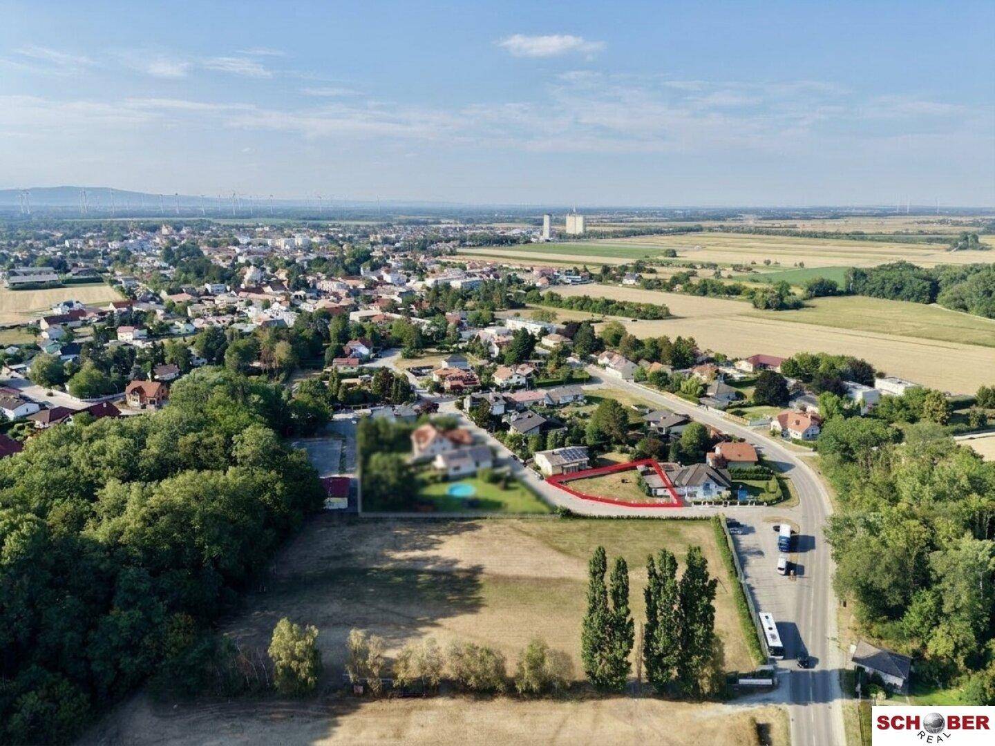 Weitläufige Luftaufnahme der Siedlung mit Feldern und einer Stadt in der Ferne, das Grundstück ist markiert.