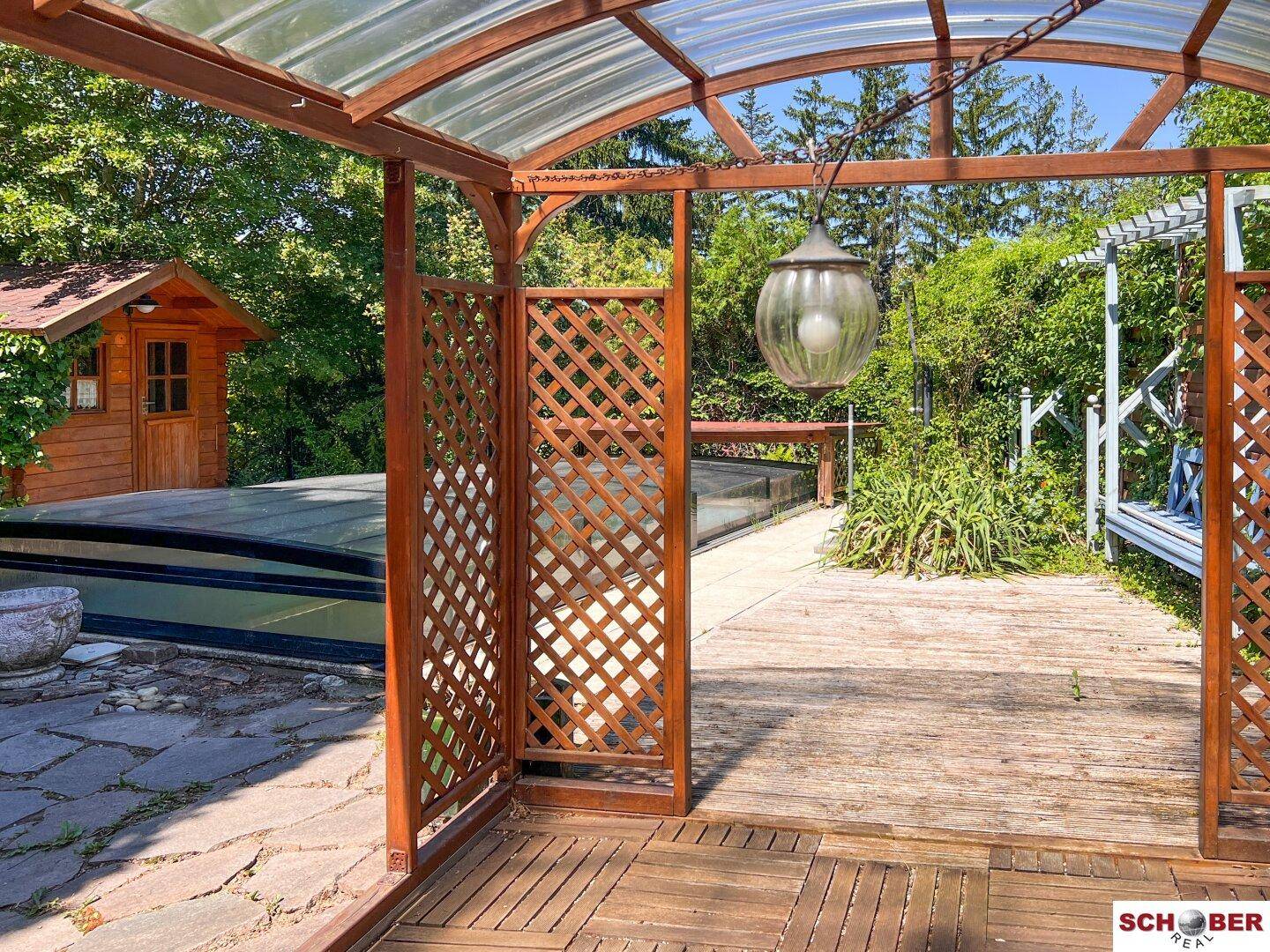 Überdachte Holzterrasse mit Blick auf den Poolbereich und Garten, ideal für Entspannung im Freien.