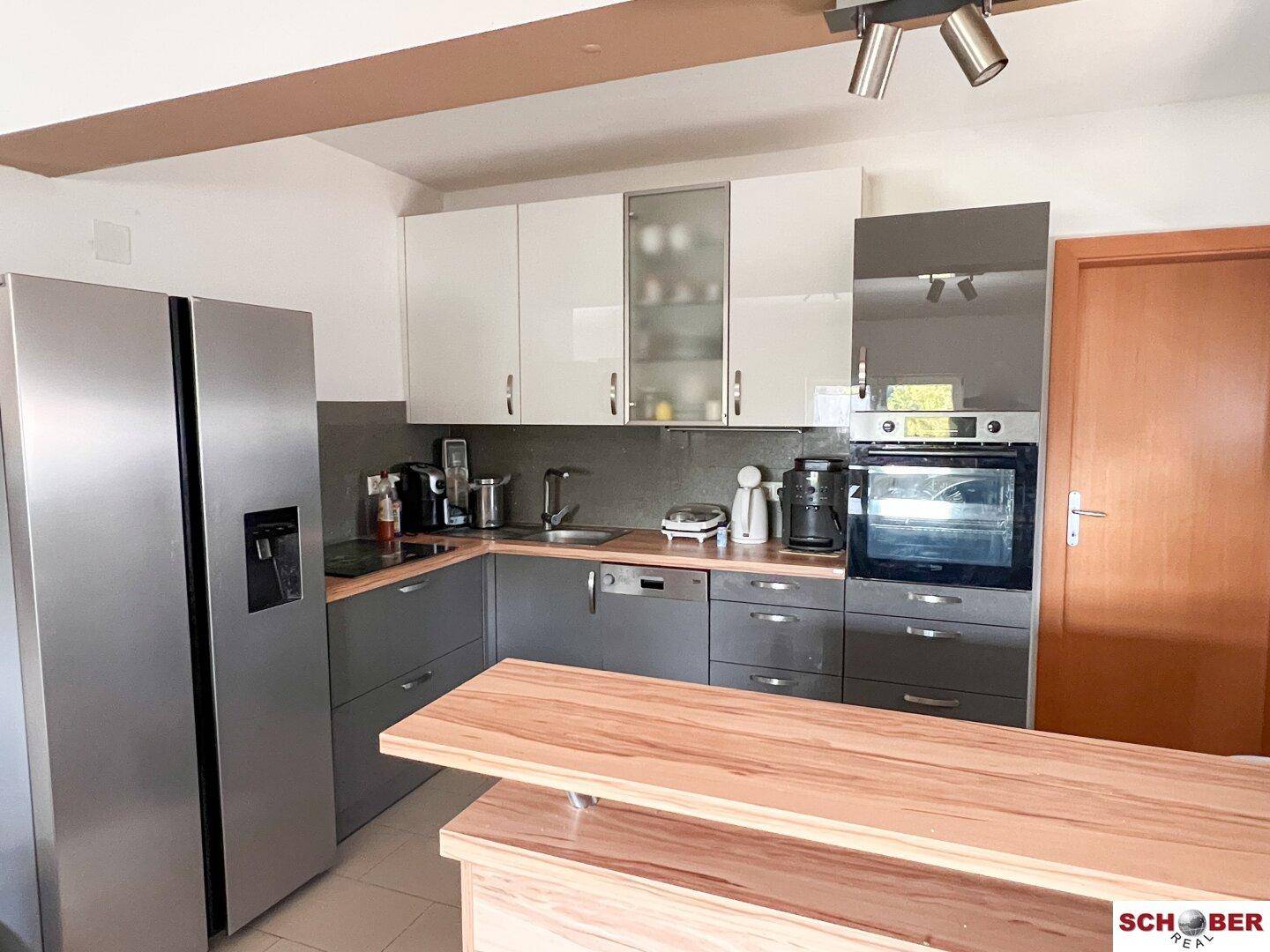 Moderne Einbauküche mit weißen und grauen Hochglanzfronten, integrierten Geräten und Kühlschrank.