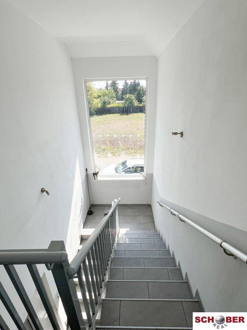 Heller Treppenaufgang mit großem Fenster und Blick ins Grüne, der die Etagen verbindet.