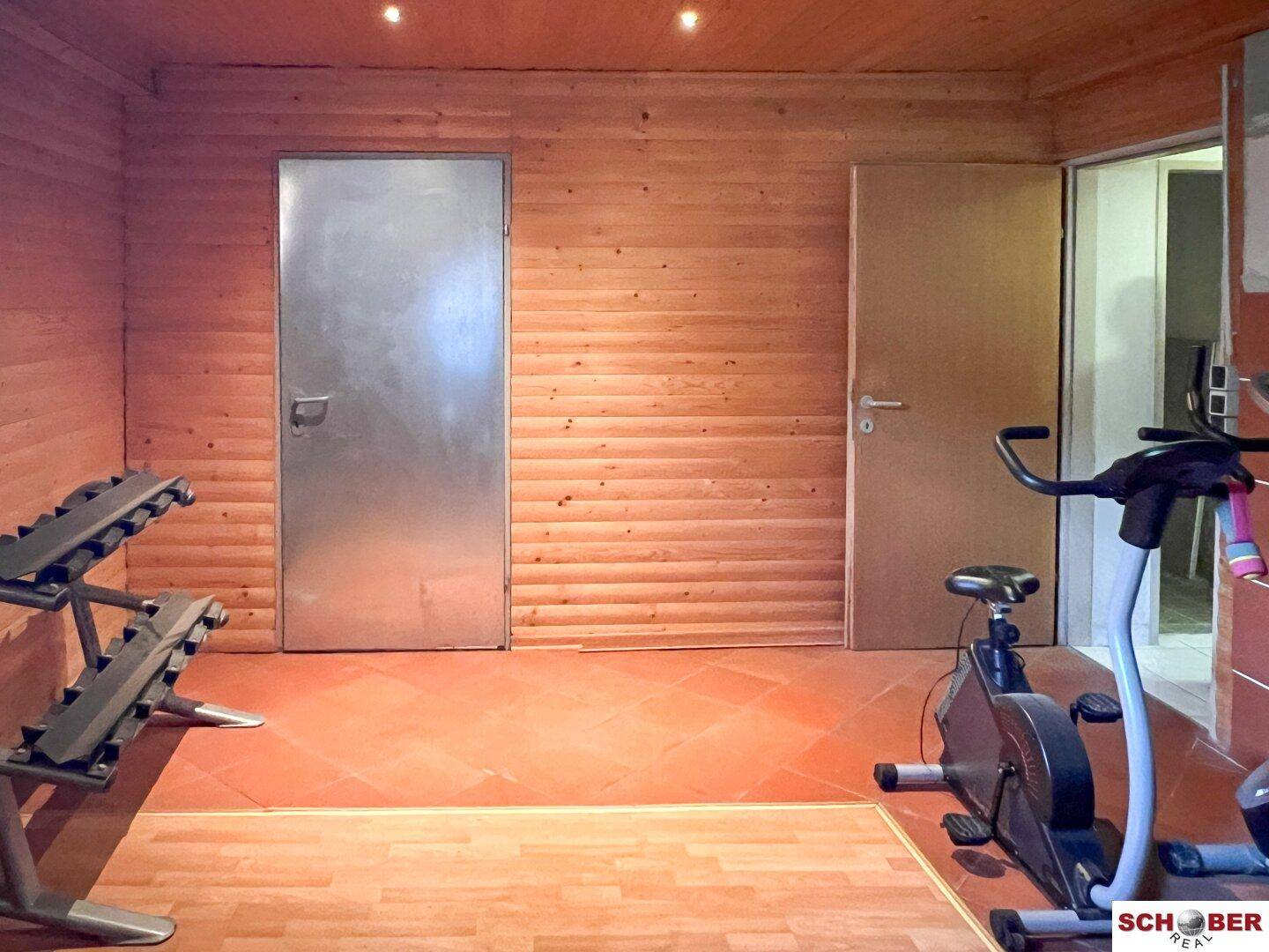 Fitnessraum mit Holzvertäfelung, Fliesenboden und grundlegenden Trainingsgeräten für sportliche Aktivitäten.