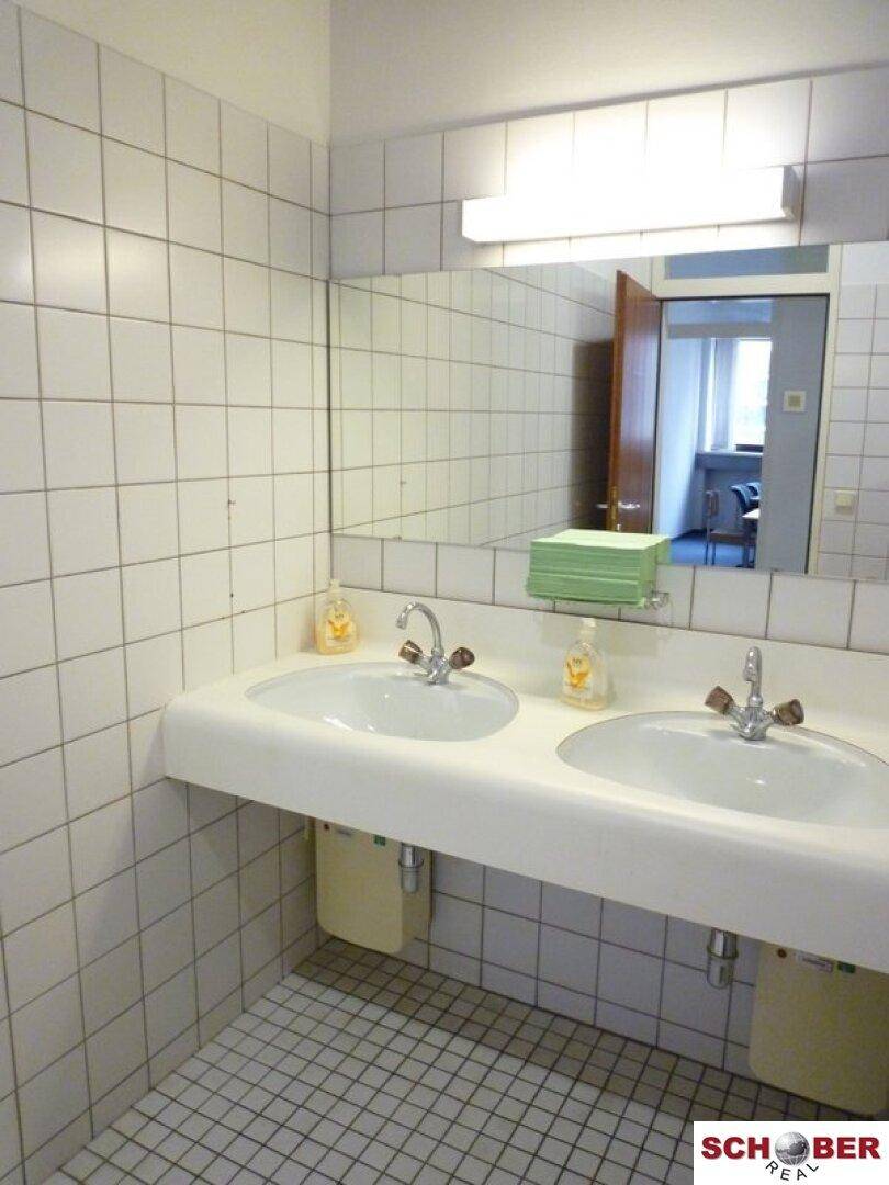 Badezimmer mit zwei Waschbecken, einem großen Spiegel und weißen Fliesen an Wänden und Boden.