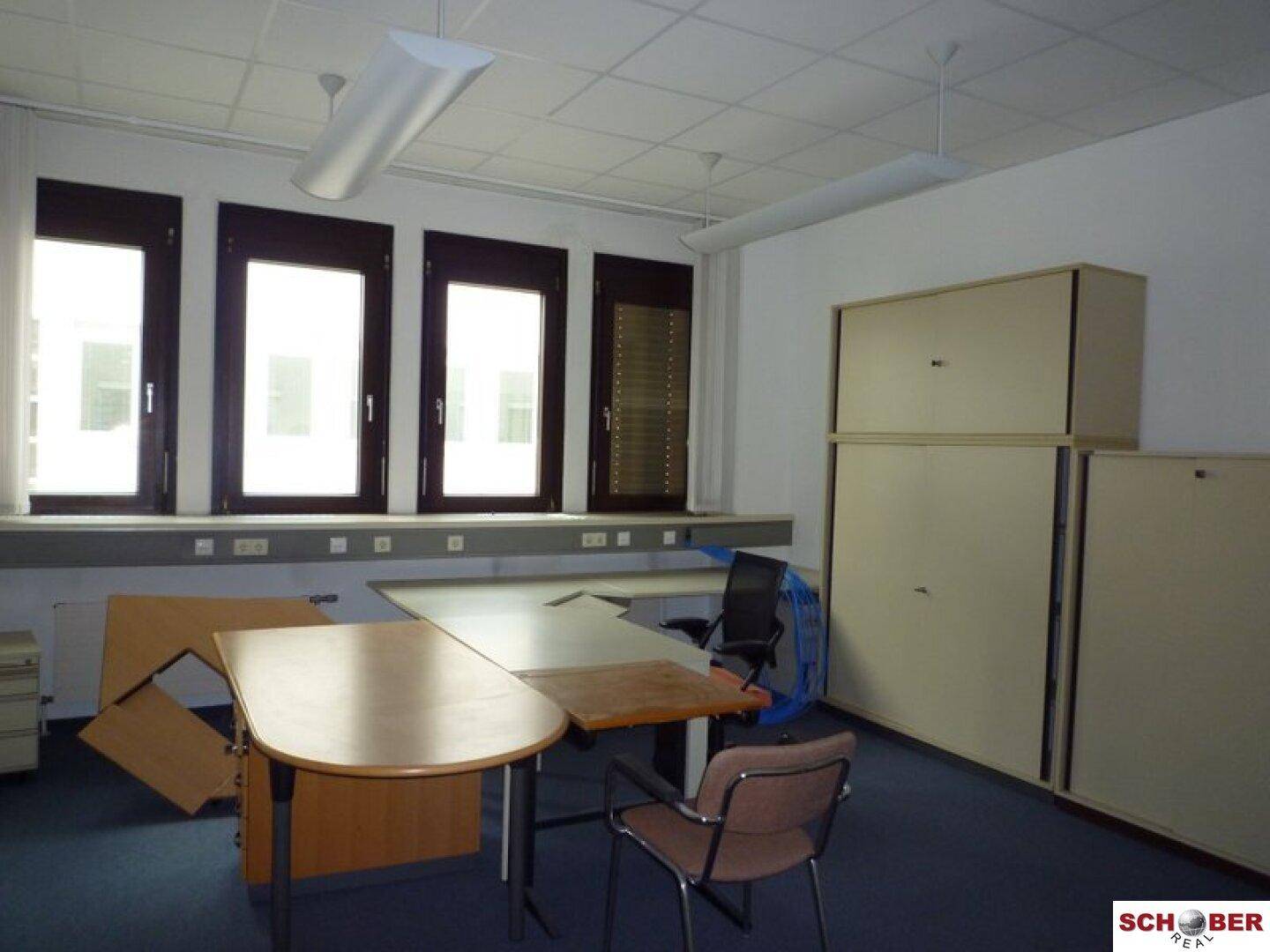 Ein Büro mit mehreren Fenstern, Teppichboden und Büromöbeln, das viel Tageslicht erhält.