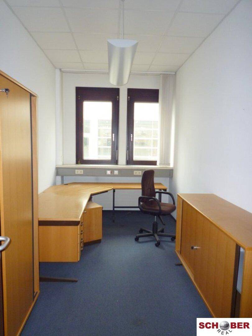 Einzelbüro mit Schreibtisch, Bürostuhl und Holzschränken, gut beleuchtet durch Fenster.