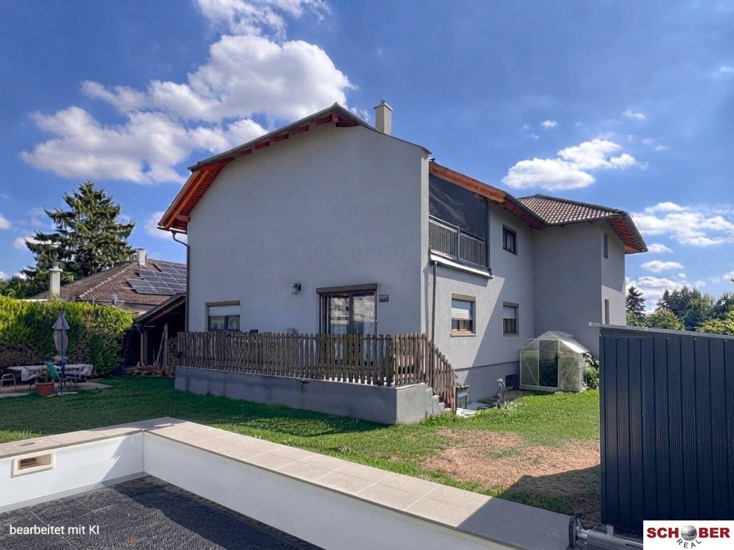 Rückansicht des Hauses mit Garten, einem Poolbereich und einem Balkon im Obergeschoss.