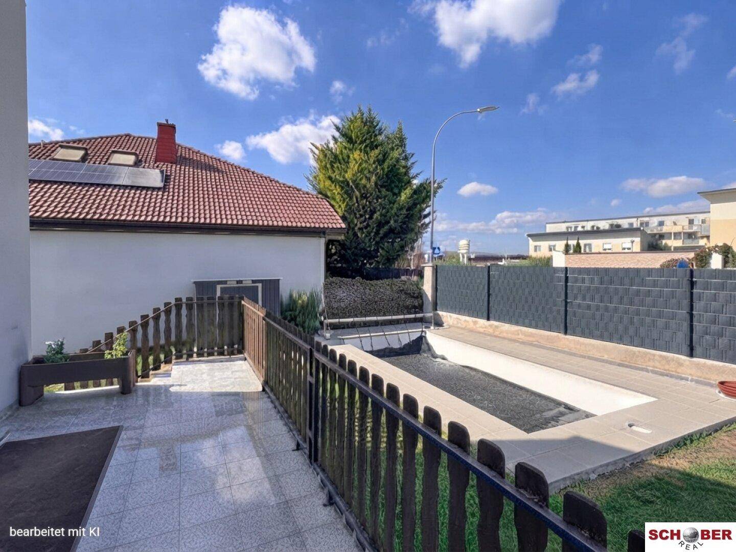 Geflieste Terrasse neben dem Poolbereich mit Blick auf die Umgebung und einen Zaun.