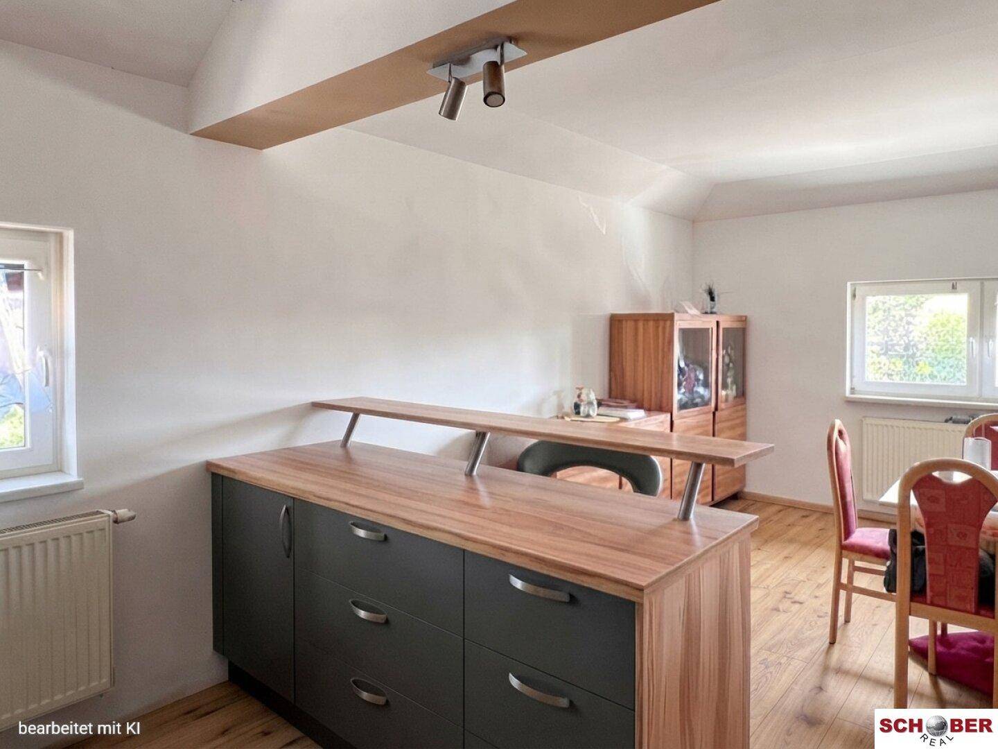 Küchenbereich mit einer modernen Kücheninsel, Holztheke und Essbereich am Fenster.