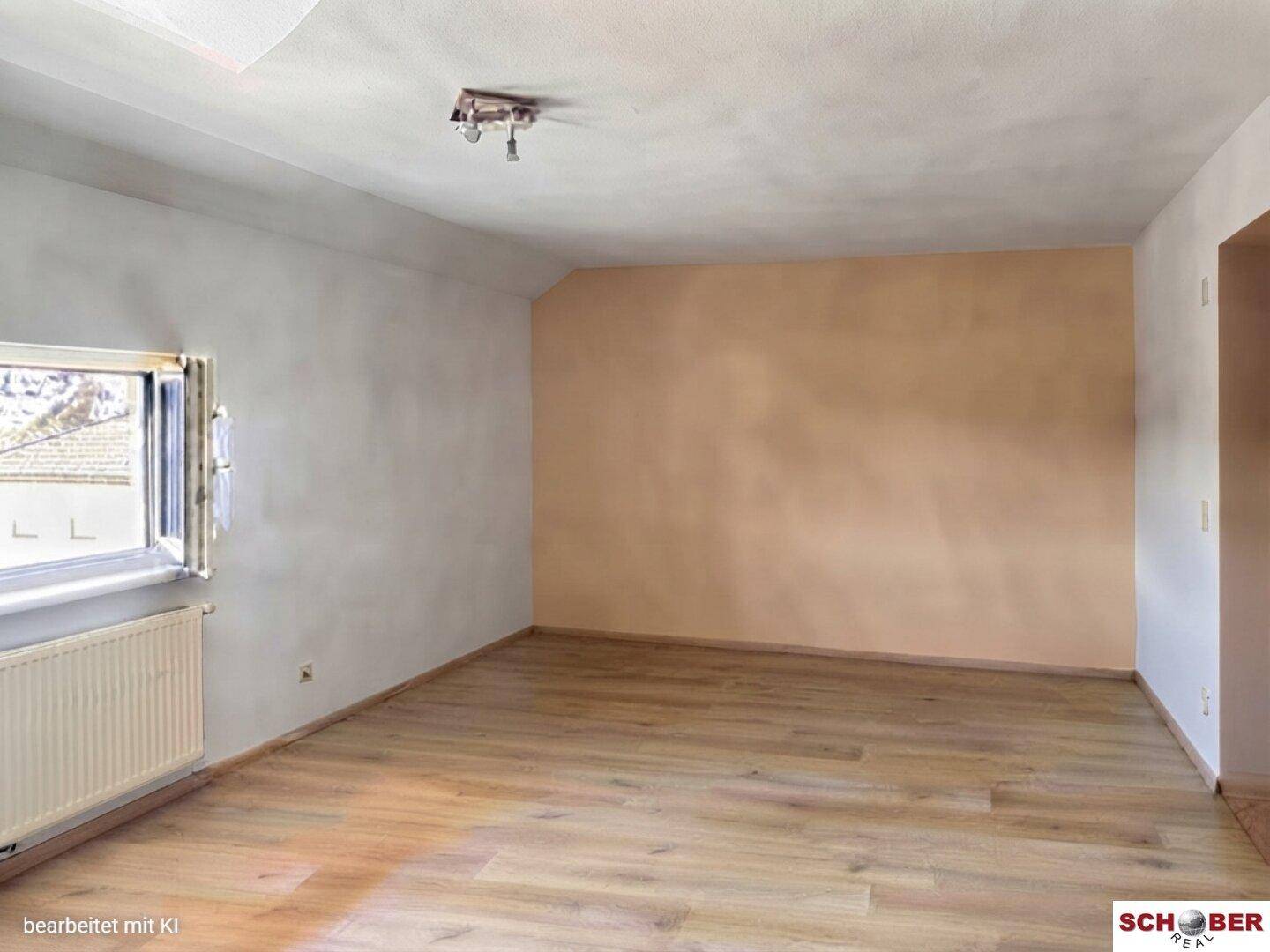 Geräumiger, heller Raum mit Laminatboden, einem Fenster und einer beigen Akzentwand.