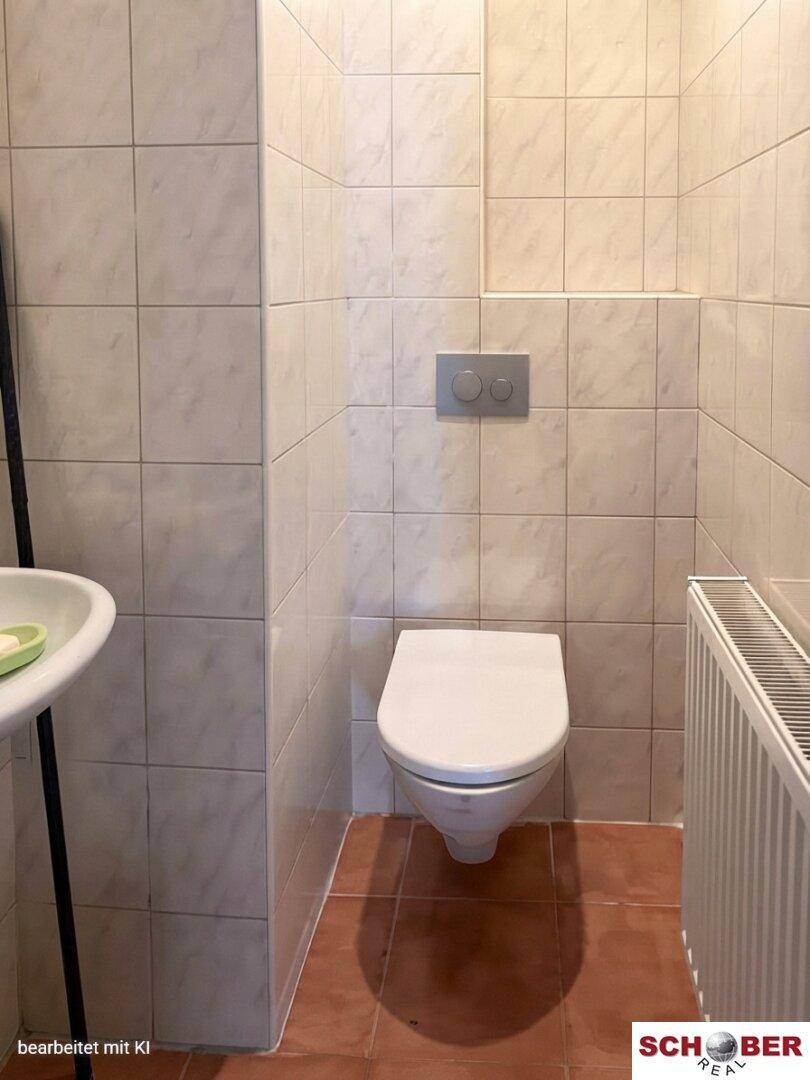 Kleines Gäste-WC mit hellen Fliesen, wandhängendem WC und einem Heizkörper.