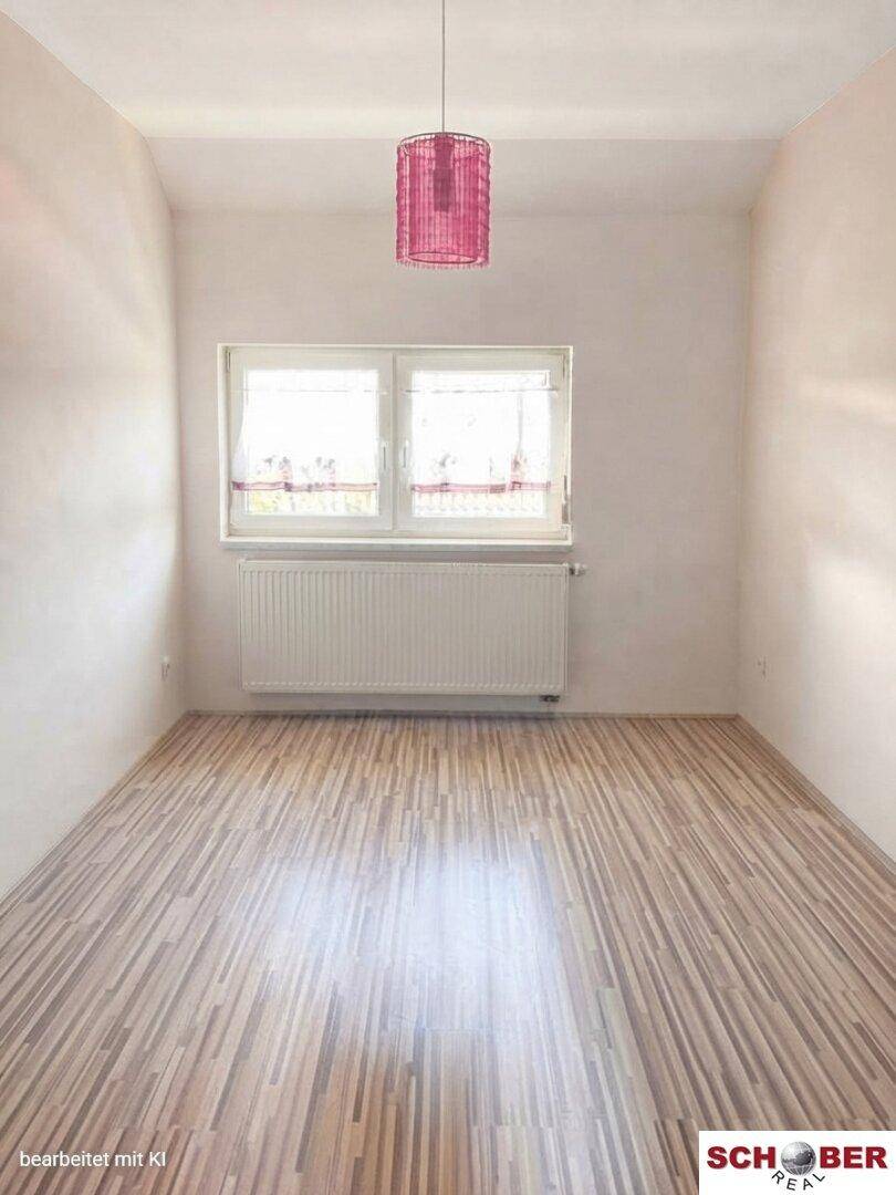 Helles Schlafzimmer mit Laminatboden, einem Fenster und einer auffälligen rosa Deckenleuchte.