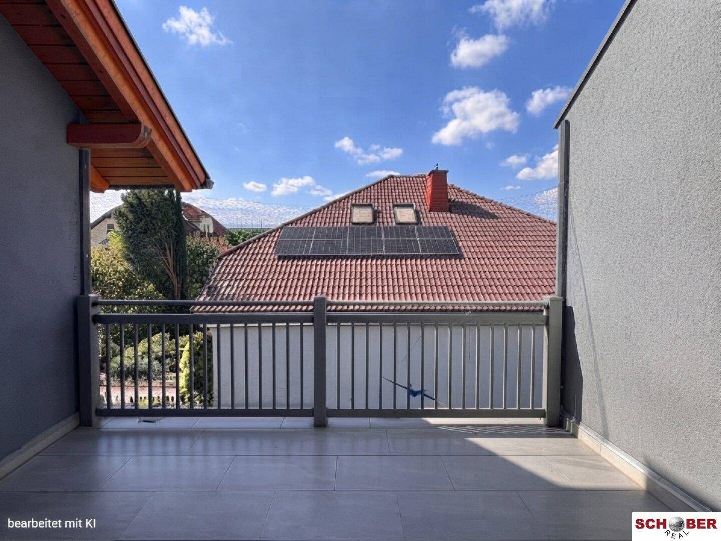 Heller Balkon mit Fliesenboden und Blick auf die Dächer der Nachbarhäuser und die Umgebung.