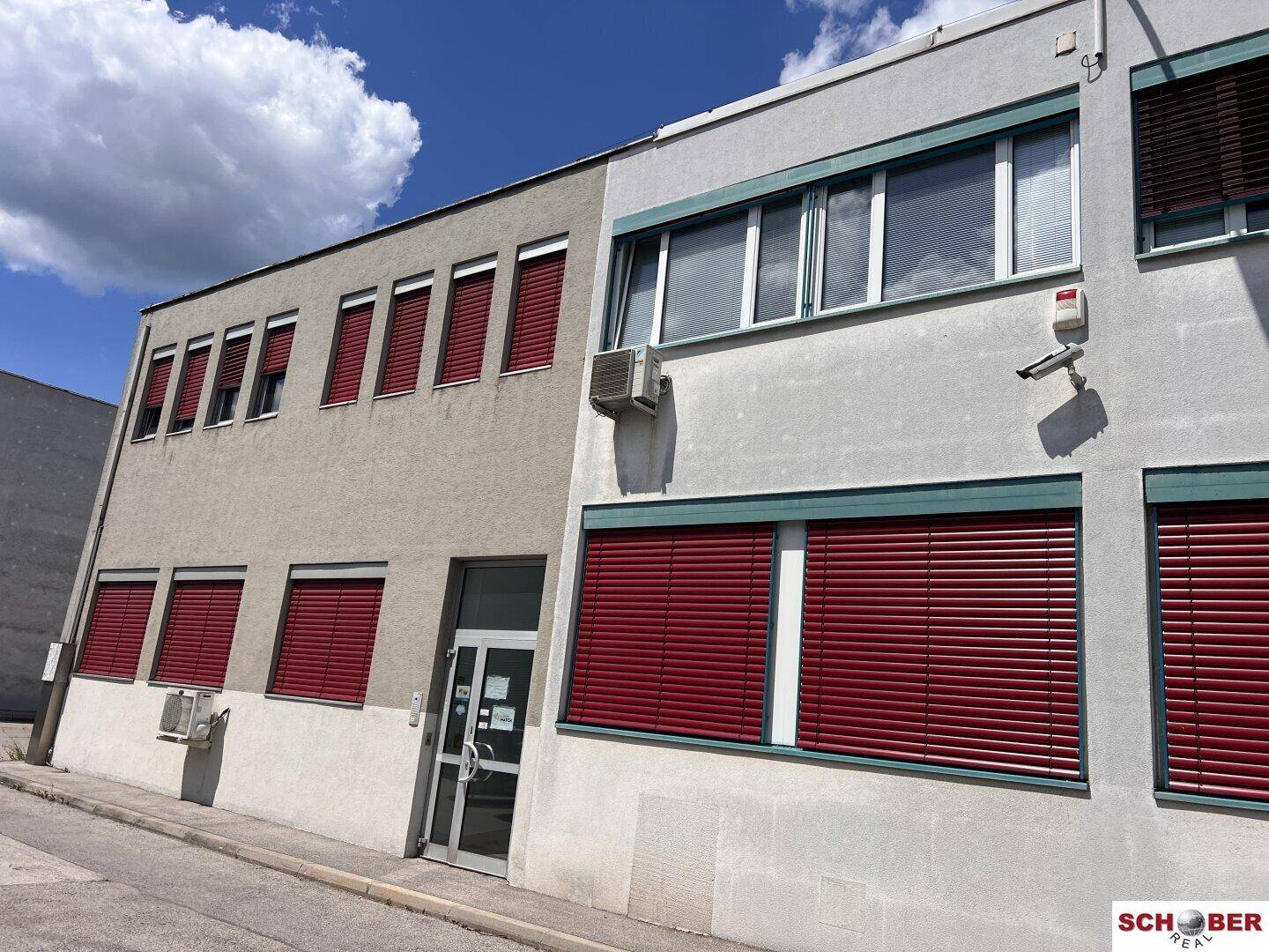 Moderne Geschäftsfassade mit großen Fenstern, roten Jalousien und Klimaanlagen.