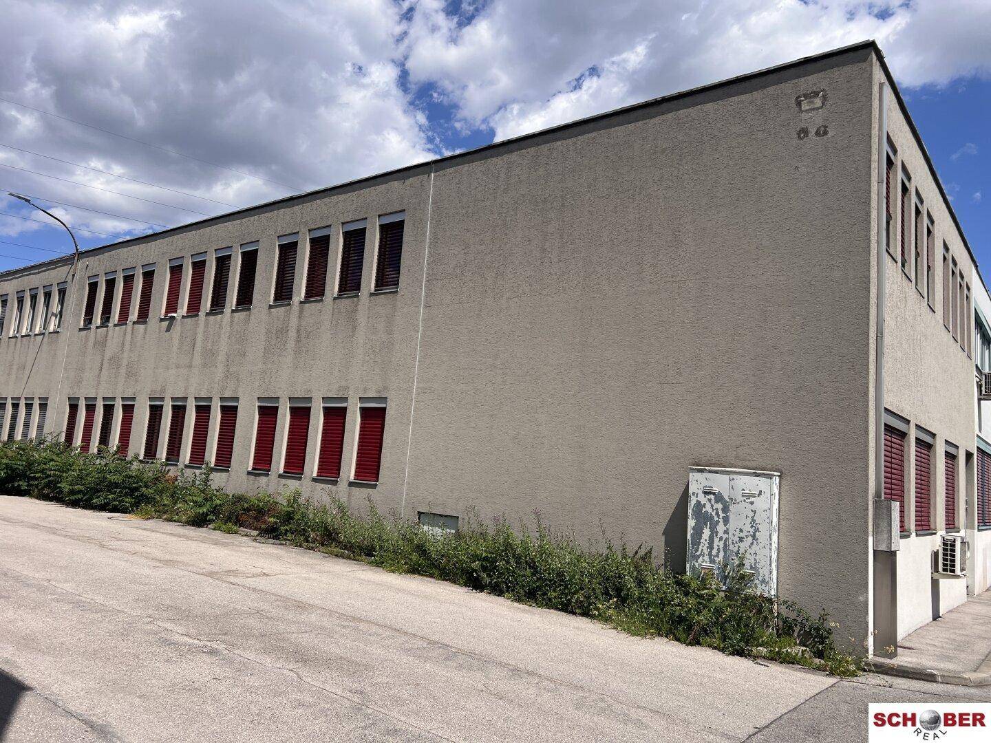 Seitenansicht eines Geschäftsgebäudes mit vielen Fenstern und roten Außenjalousien.