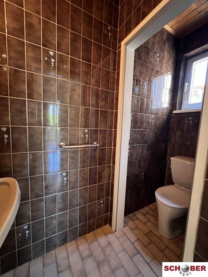 Kleines WC mit braunen Fliesen an Wänden und Boden, ausgestattet mit Toilette und Waschbecken.