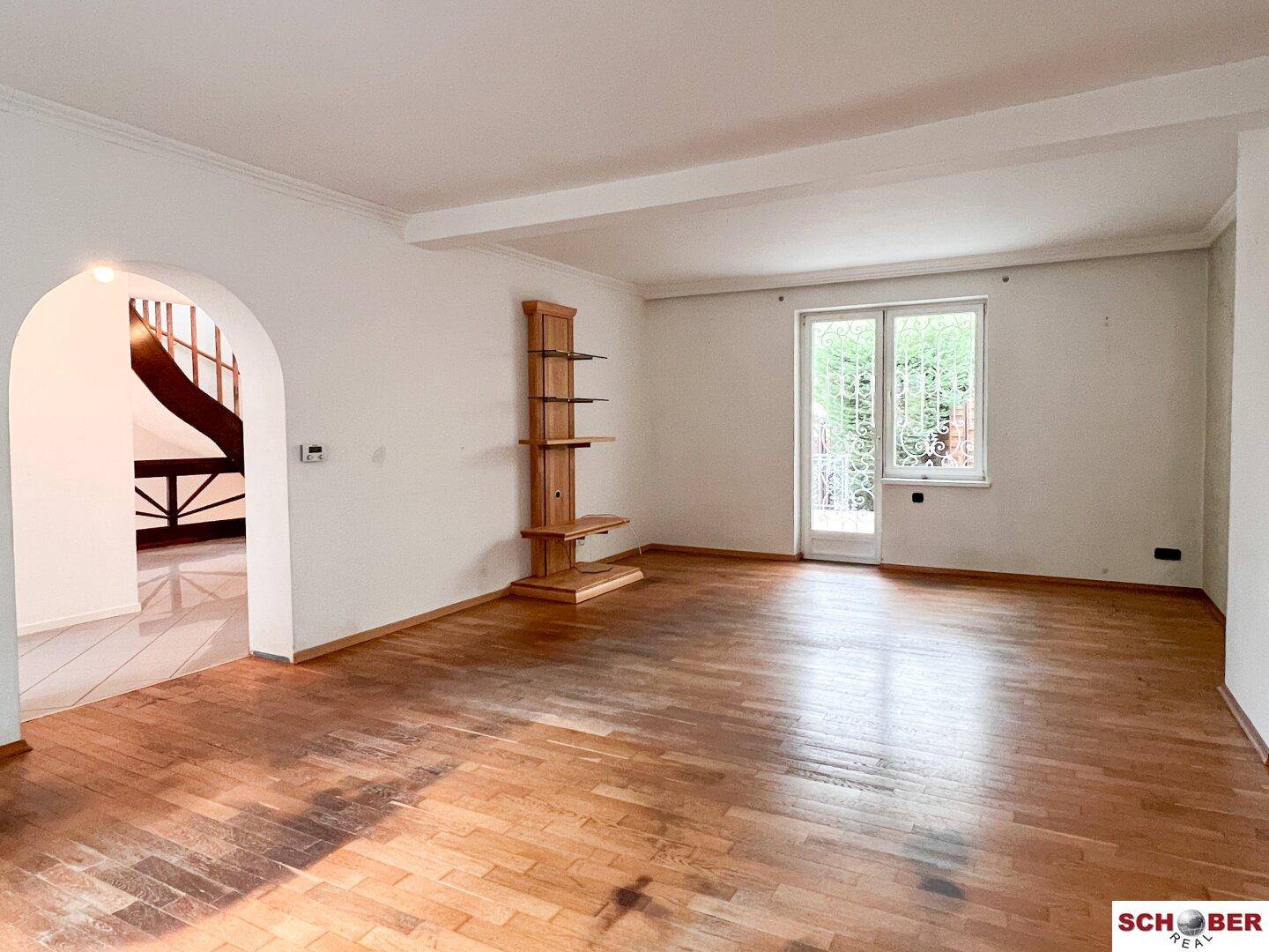 Geräumiges Wohnzimmer mit Holzboden, weiß gestrichenen Wänden und Zugang zu einem Außenbereich.