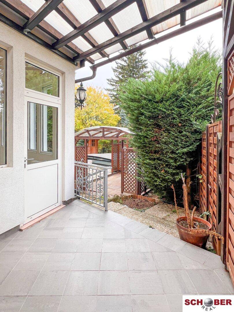 Gedeckte Terrasse mit Fliesenboden, Metallgeländer und Blick auf den Gartenbereich mit Pavillon.
