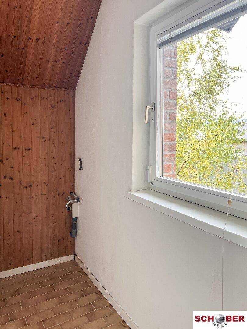 Kleiner Hauswirtschaftsraum mit Holzverkleidung, Fenster und sichtbaren Wasseranschlüssen.