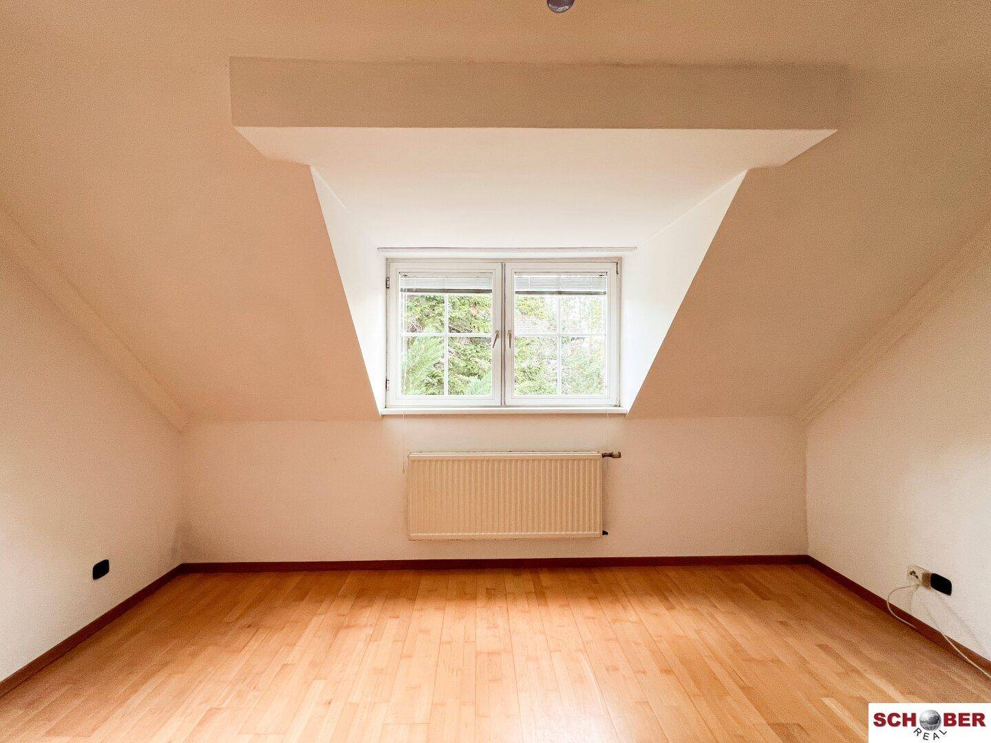Dachzimmer mit Laminatboden, schrägen Wänden und einem großen Dachgaubenfenster.