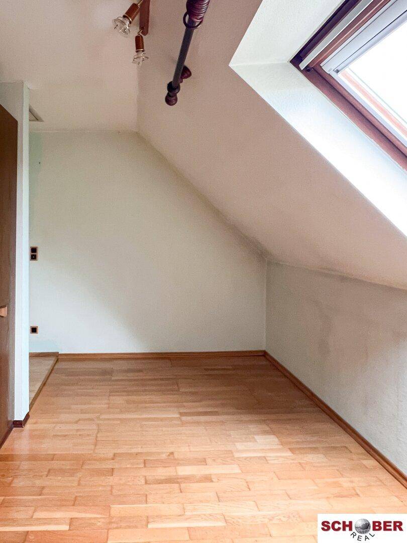 Dachzimmer mit Laminatboden, schrägen Wänden und einem Dachfenster für natürliches Licht.
