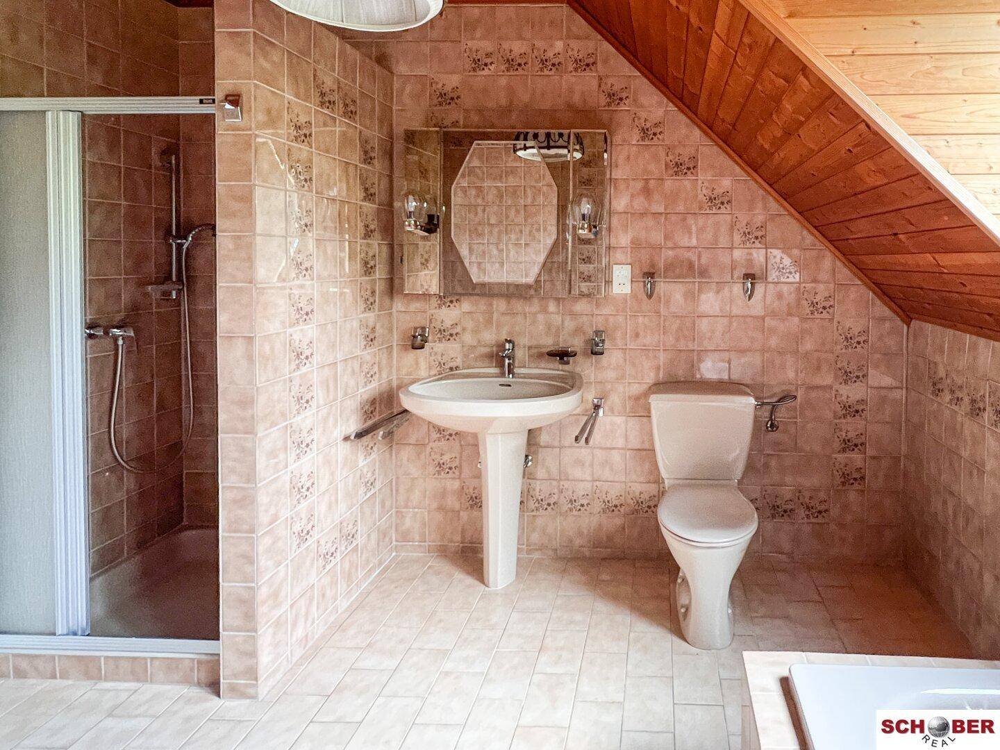 Badezimmer im Dachgeschoss mit Dusche, WC, Waschbecken und beigefarbenen Fliesen.