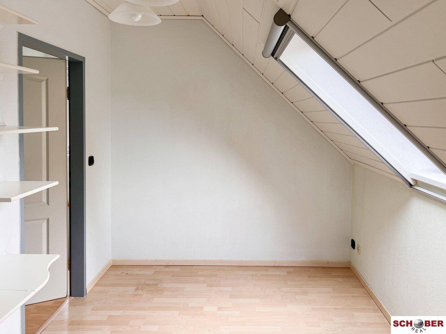 Helles Dachzimmer mit Laminatboden, schrägen Wänden und einem Dachfenster.