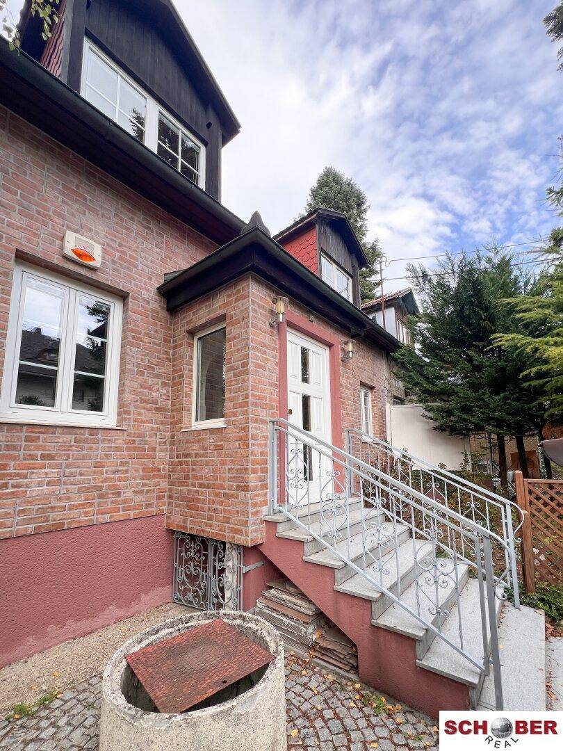 Vorderansicht eines Backsteinhauses mit Eingangstreppe, Fenstern und einem kleinen Vorgarten.