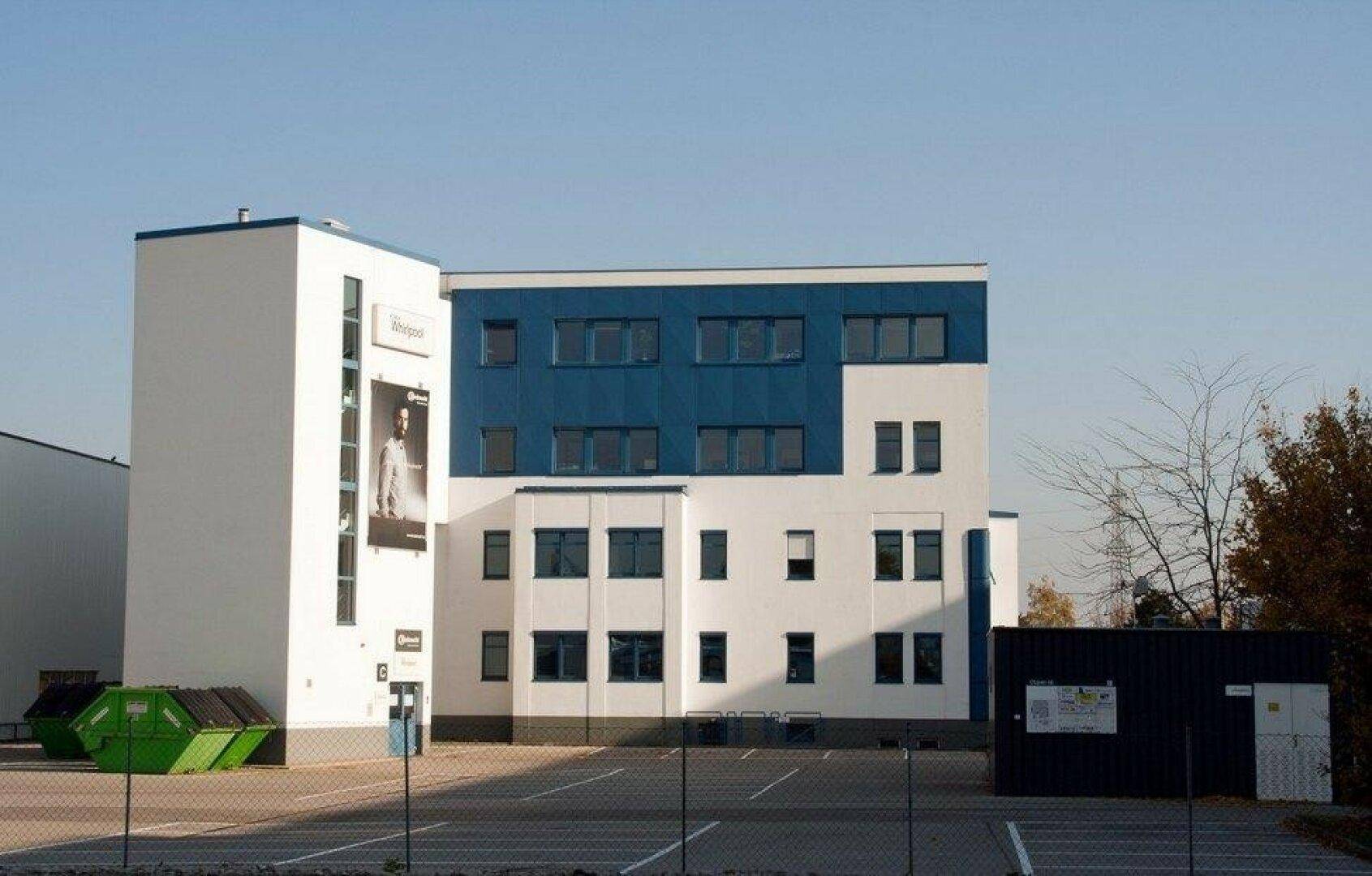Modernes Geschäftsgebäude mit blau-weißer Fassade und angrenzendem Parkplatz unter klarem Himmel.