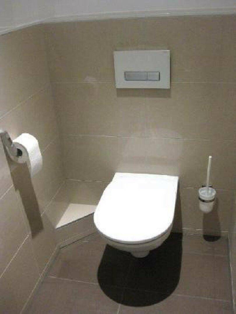 Saubere Toilette mit Wand-WC und Fliesen an Wänden und Boden in neutralen Farbtönen.