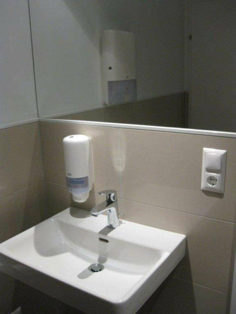 Modernes Waschbecken mit Seifenspender und Spiegel in einem hell gefliesten Badezimmer.