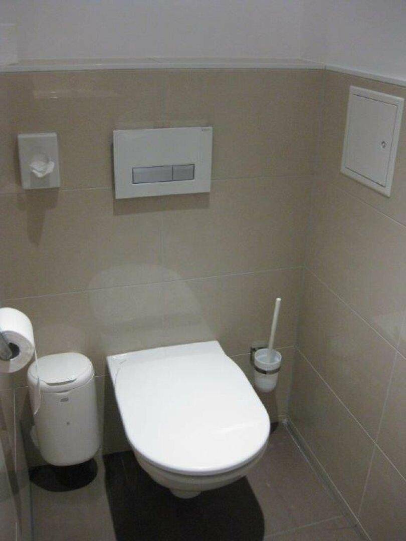 Wandhängendes WC mit Spülkasten und Fliesen an den Wänden in einem sauberen Badezimmer.