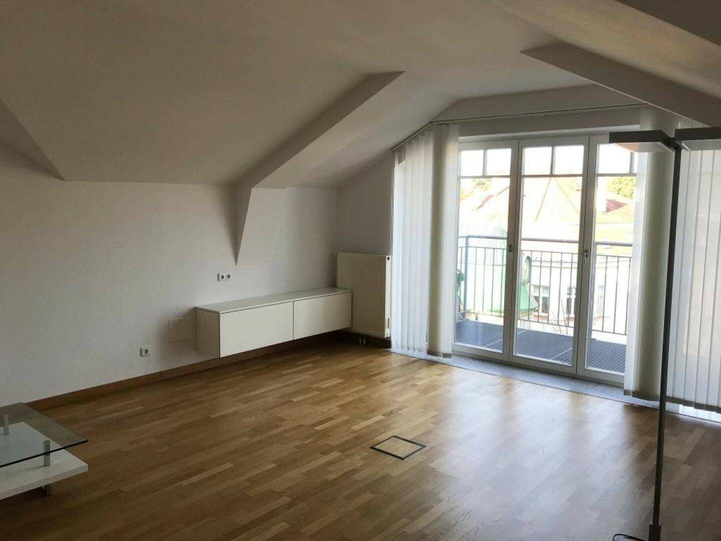 Heller, leerer Raum im Dachgeschoss mit schwebendem Sideboard und Zugang zu einem Balkon.