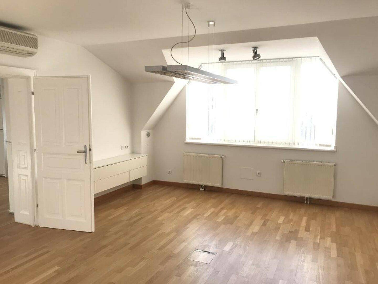 Leerer Raum im Dachgeschoss mit großem Fenster, Holzboden und schwebendem Sideboard.