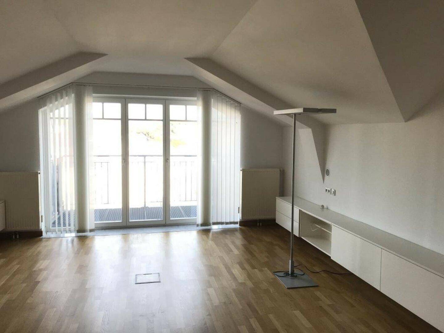 Heller, leerer Raum mit Balkontür, schwebendem Sideboard und Stehlampe.