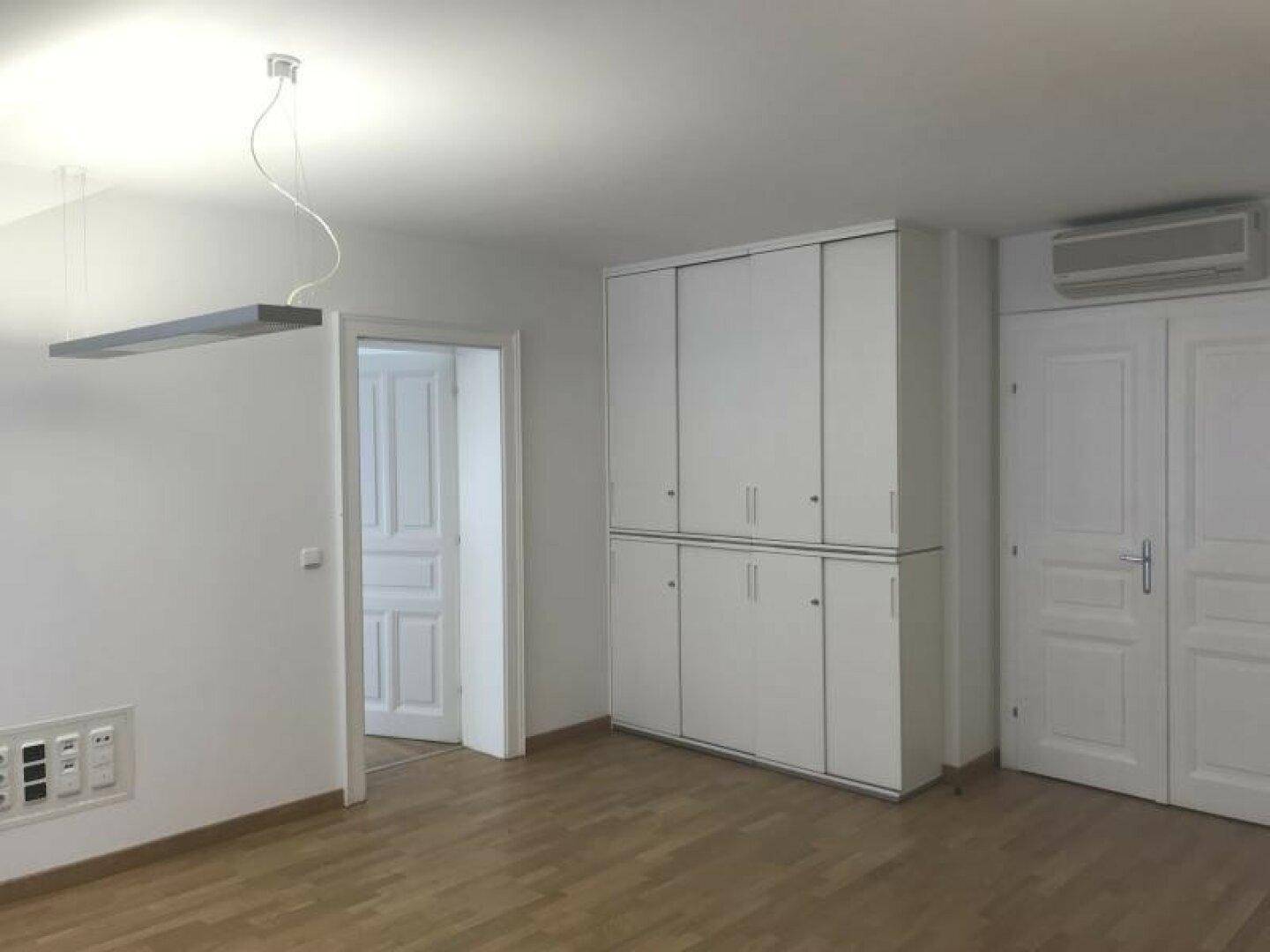 Leerer Raum mit großem weißen Einbauschrank, Klimaanlage und Holzboden.