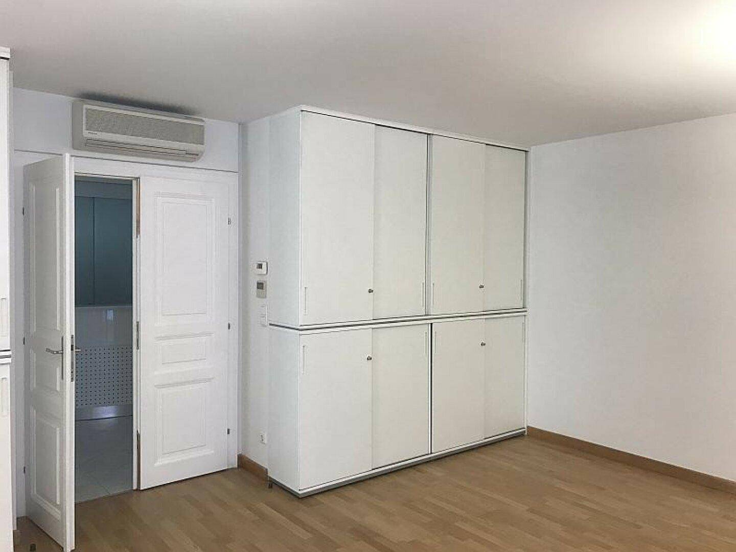 Heller, leerer Raum mit großem weißen Einbauschrank, Klimaanlage und Holzboden.