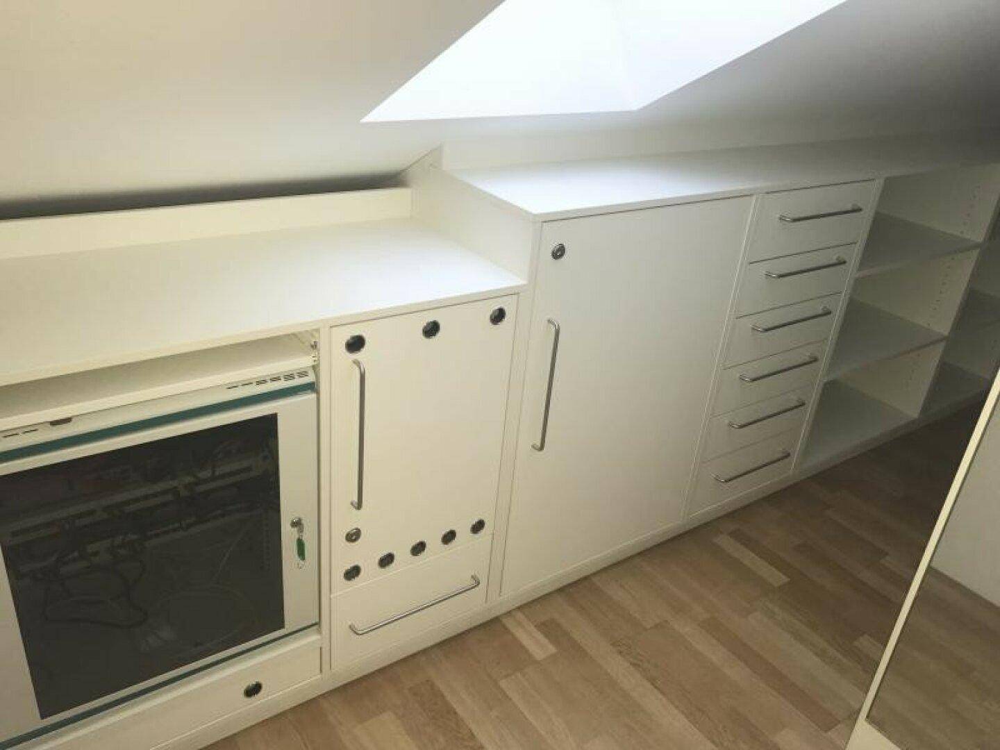 Maßgefertigte weiße Einbauschränke und Schubladen unter einer Dachschräge mit Oberlicht.