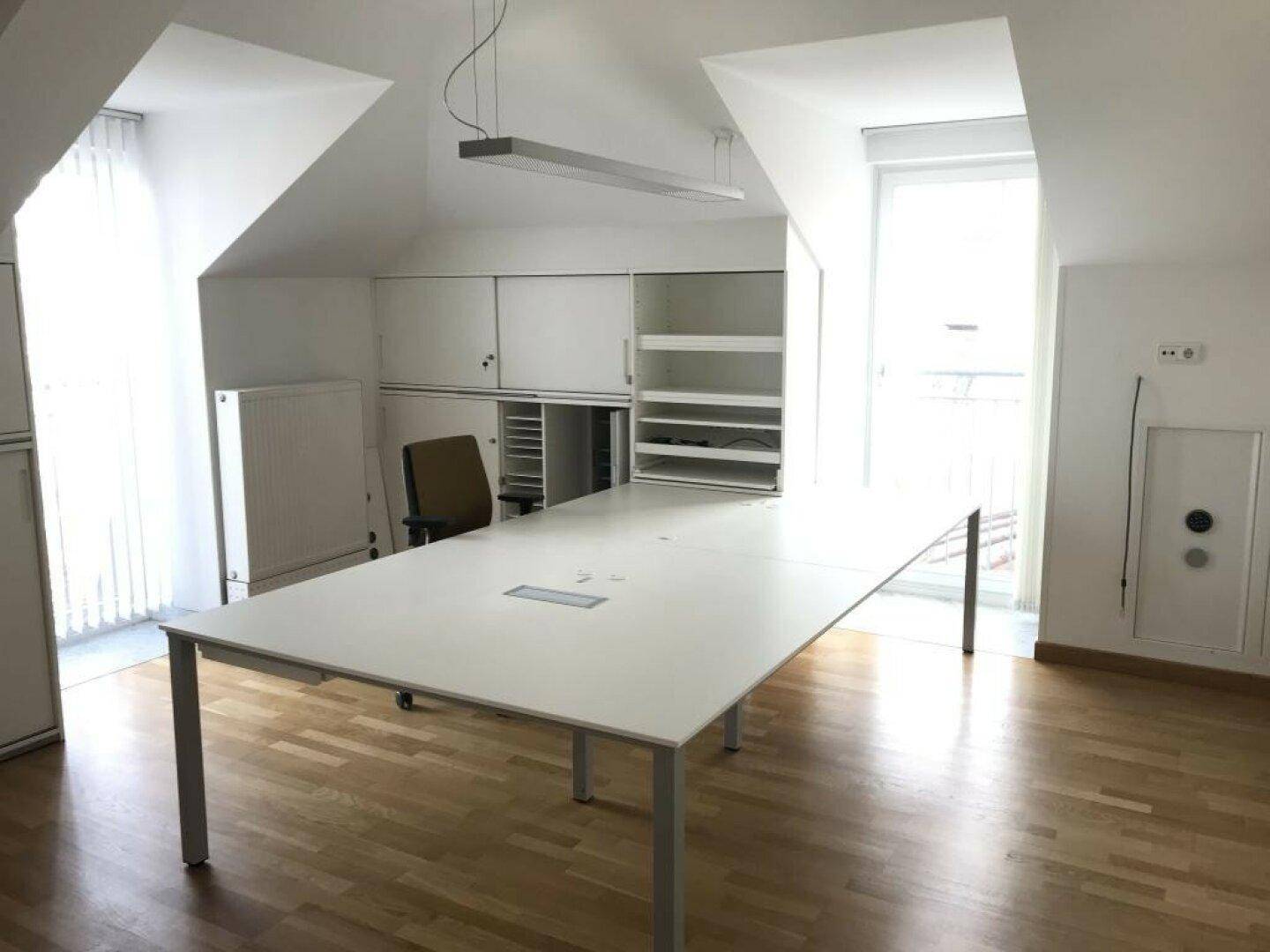 Großer leerer Raum mit einem langen weißen Tisch, Einbauschränken und Dachschräge.