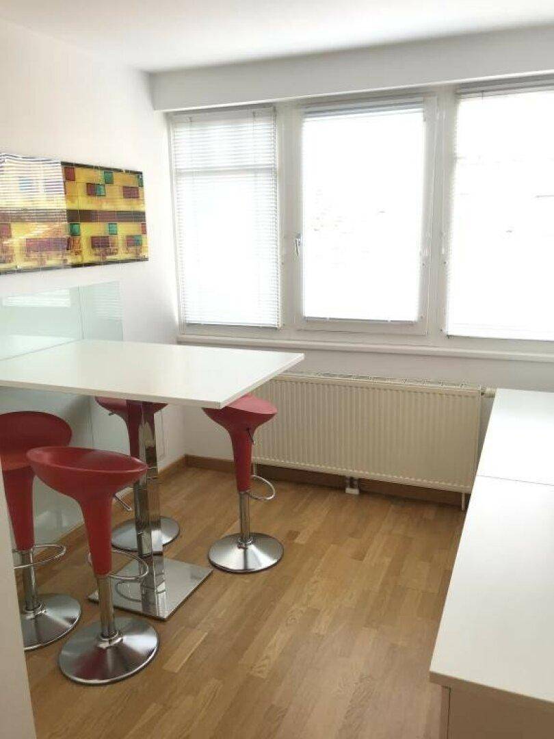 Kleiner Essbereich oder Pausenraum mit weißem Tisch, roten Barhockern und Fenster.
