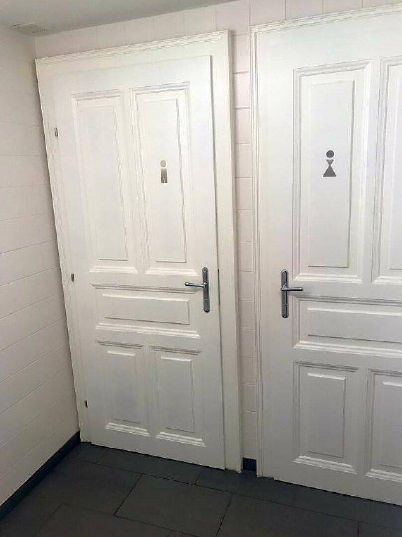 Zwei weiße Türen mit Geschlechtssymbolen, die zu den Toiletten führen.